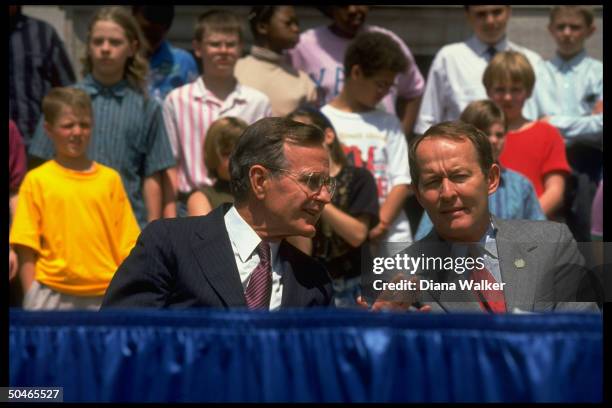 Pres. Bush sitting outside w. Education Secy. Lamar Alexander , conferring, framed by kids, during fete at St. Paul Public Library .