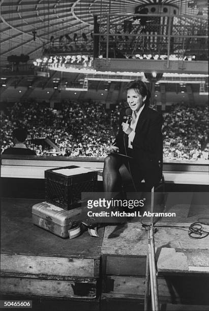 Sportscaster Andrea Joyce w. Mike, reporting at halftime of Notre Dame/Seton Hall basketball game from barren area overlooking basketball court at...