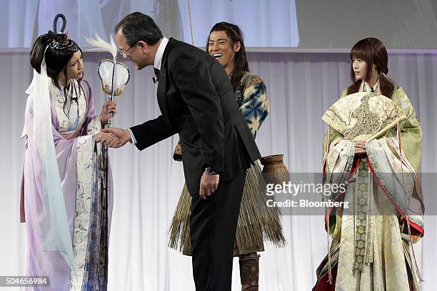 Takashi Tanaka, president of KDDI Corp., second left, shakes hands with model and actress Nanao, left, while actor Kenta Kiritani, second from right,...