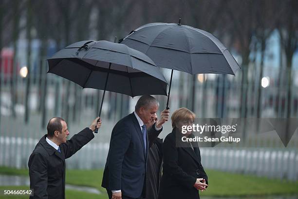 German Chancellor Angela Merkel and Algerian Prime Minister Abdelmalek Sellal walk under umbrellas as they prepare to review a guard of honour upon...