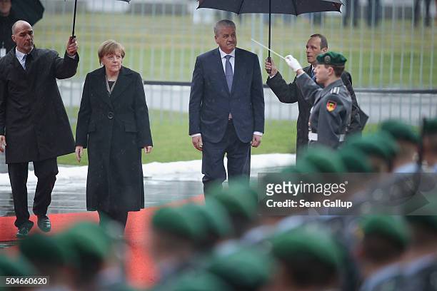 German Chancellor Angela Merkel and Algerian Prime Minister Abdelmalek Sellal walk under umbrellas as they review a guard of honour upon Sellal's...