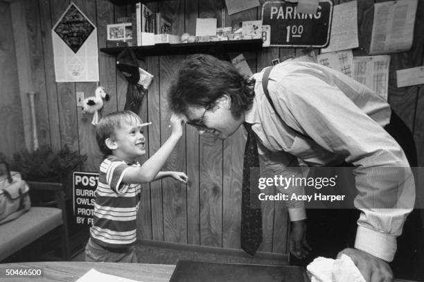 Mike Veeck, pres. Of Miracle, a minor-league baseball team, bending over while his 5-yr-old son William Night Train pulls a suction cup dart off his...