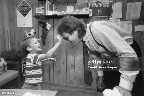 Mike Veeck, pres. Of Miracle, a minor-league baseball team, bending over while his 5-yr-old son William Night Train pulls a suction cup dart off his...