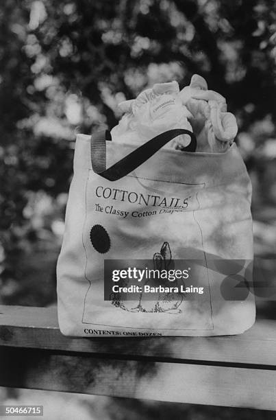 Closeup of a canvas carry-all bag emblazoned w. Rabbit logo for COTTONTAILS, the Classy Cotton Diaper, overflowing w. Several diapers from the dozen...