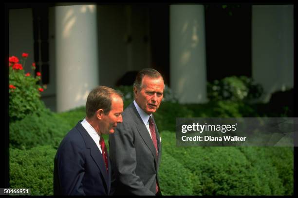 Pres. Bush strolling w. Education Secy. Lamar Alexander, framed by foliage, in verdant WH Rose Garden.