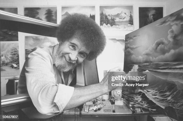 Painting instructor/artist Bob Ross using a large paint brush to touch up one of his large seascapes in his studio at home.