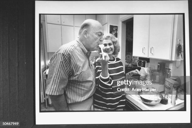 Author Anne Rivers Siddons letting her husband Heywood taste the broccoli casserole she is mixing in a bowl in her kitchen at home.