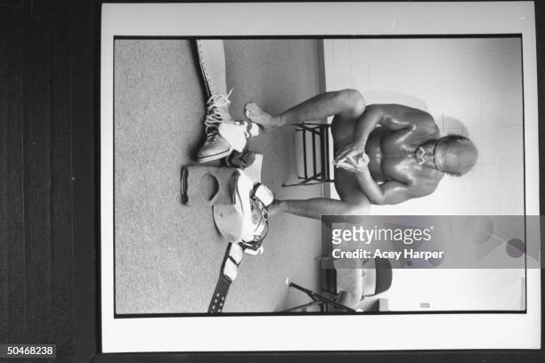 Wrestler Hulk Hogan glistening w. Sweat as he sits almost nude on chair after disrobing from his wrestling togs which lie in a pile on the floor in...