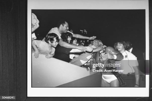 Wrestler Hulk Hogan in his wrestling togs, holding his championship belt as he is hugged & greeted by exuberant fans at ringside after his bout at...