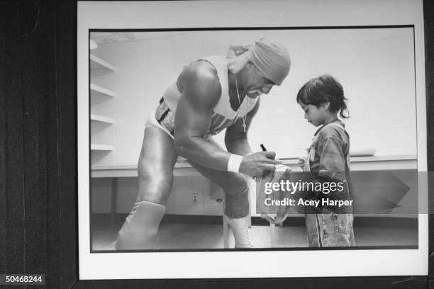 Wrestler Hulk Hogan in wrestling togs, signing autograph for a small youngster in dressing room before bout at the Miami Arena.