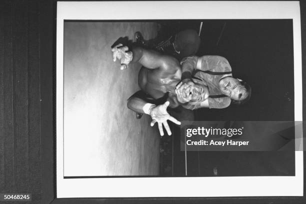 Wrestler Hulk Hogan grimacing in agony as wrestler Sargeant Slaughter holds his chin in a headlock while sitting on his back in the ring during their...