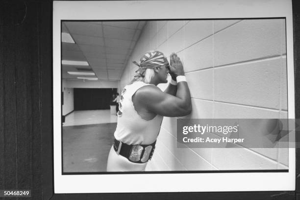 Wrestler Hulk Hogan leaning w. His forehead against his clasped hands while praying against wall in hallway before his wrestling match at Miami Arena.