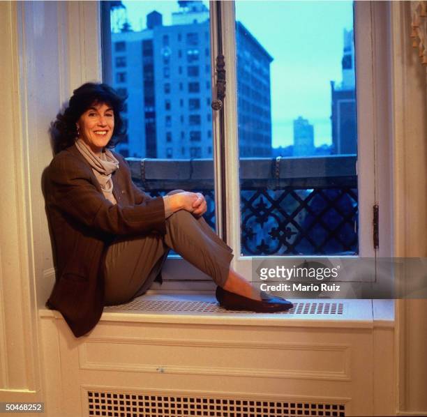 Writer Nora Ephron sitting on window sill/radiator, w. Cityscape view.