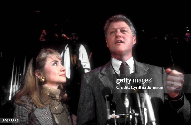 Gov. & Dem. Presidential candidate Bill Clinton speaking into mikes at fundraiser while wife Hillary stands loyally by his side.