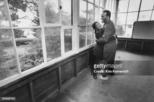 Actor Danny Glover hugging his wife Asake Bomani on large glassed-in porch.