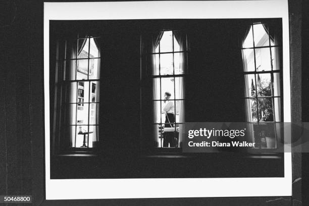 Adv. Brent Scowcroft in shirt-sleeves, talking on phone while standing in his WH office at night as seen from outside, looking in through large...