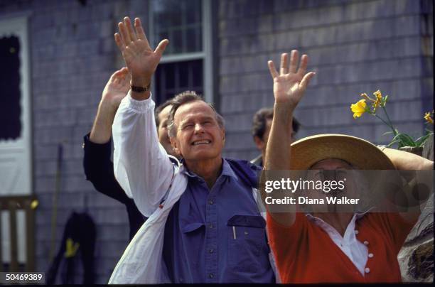 Pres. & Barbara Bush waving goodbye , w. 1st Lady onto her beachcomber straw hat as Marine One raises gust.