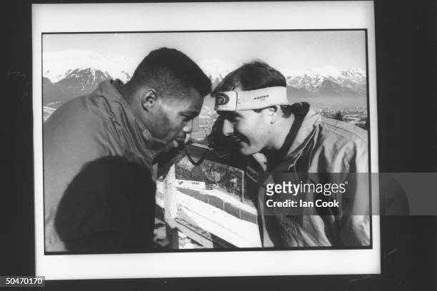 Blobsled teammates , football star Herschel Walker & ex-skier Randy Will, posing head-to-head as they listen to tourist telephones on deck of ski...