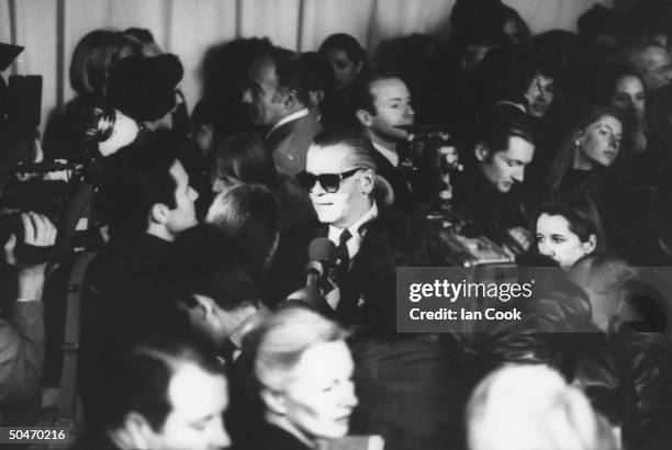 Fashion designer Karl Lagerfeld facing crowd & press holding mikes & cameras at Chanel spring show.