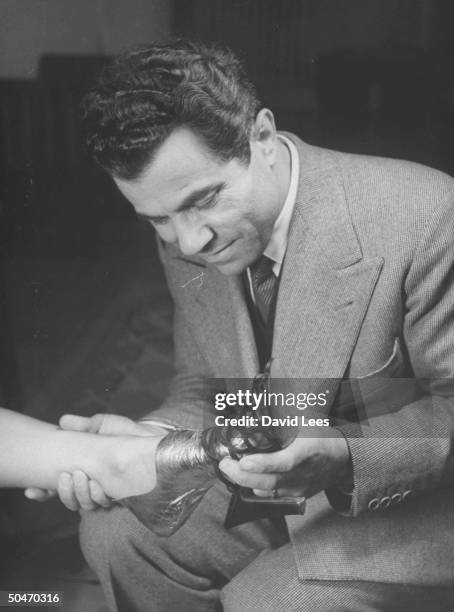 Shoe designer Salvatore Ferragamo slipping strappy mule shoe on woman client's foot, which is wrapped in protective bootie.