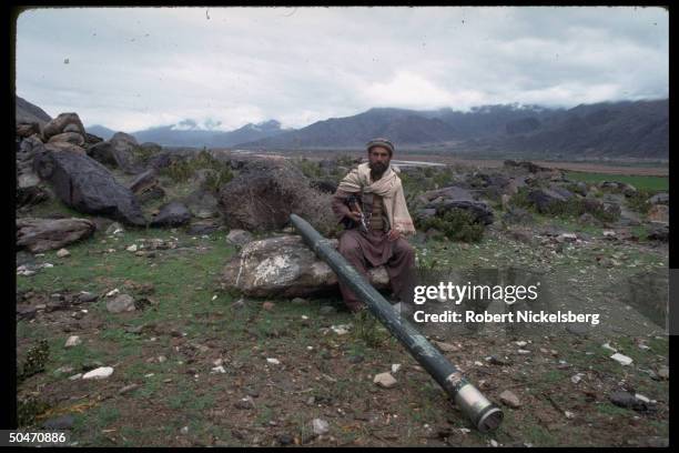 Ethnic Pathan mujahedin fighter sitting, sharing rock w. Propped rocket weapon in Salafiya rebel-controlled Kunar province.