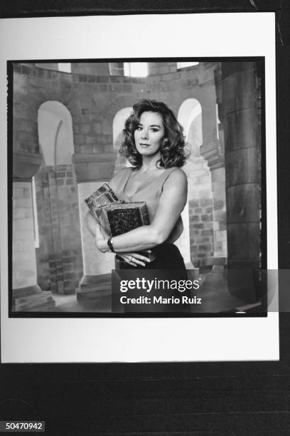 Actress Paige O'Hara craddling three books in her arms in front of backdrop at studio, acting like the character Belle, the book lover, for whom she...