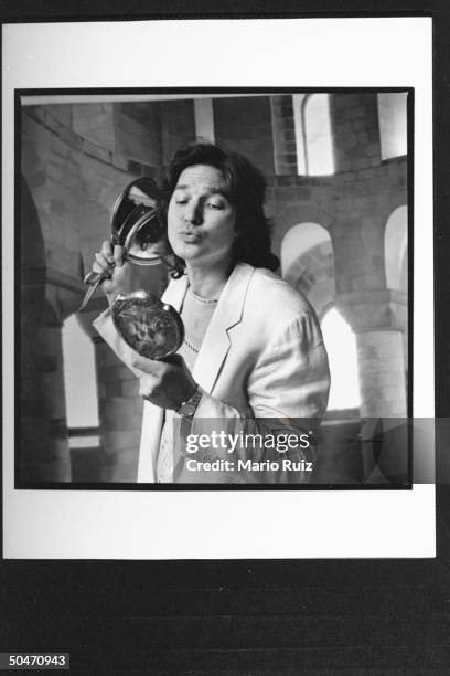 Actor Richard White admiring himself in hand mirror as he holds two others in front of backdrop at studio, acting like the character Gaston for whom...