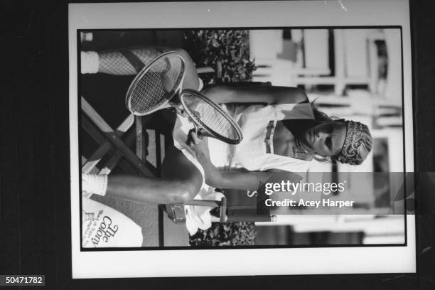 Tennis player Carling Bassett-Seguso wearing white tennis dress as she inspects two of her tennis racquets while sitting courtside during a break in...
