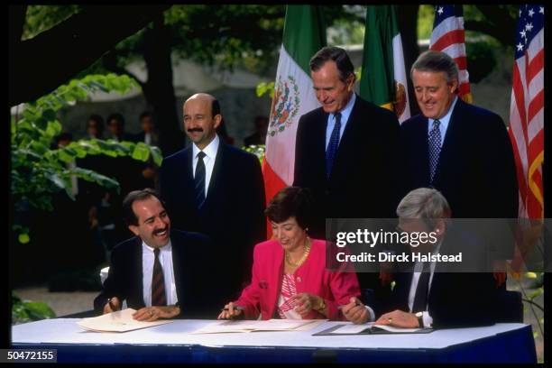 Presidents Mulroney, Bush & Salinas de Gortari standing over respective reps. Wilson, Hills & Serra Puche at N. Amer. Free Trade Agreement treaty...