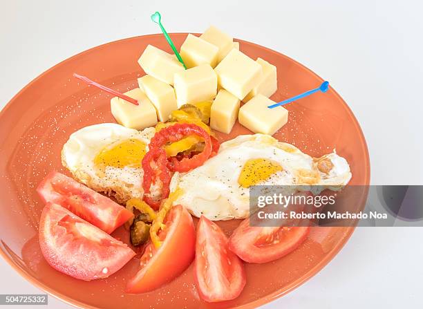 Cuban breakfast : Egg,cheese cubes with heart shaped toothpicks and tomatoes with black pepper sprinkled served in brown plate.