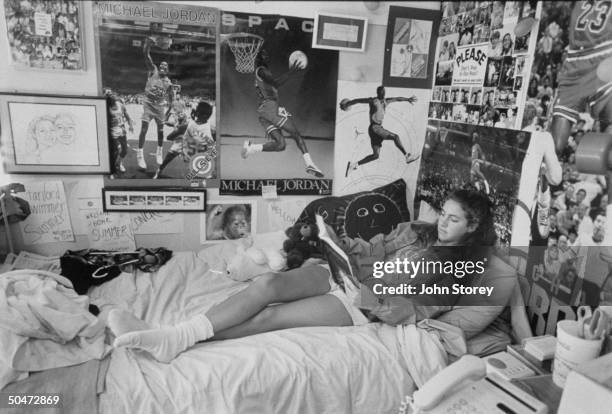 Olympic swimmer Summer Sanders studying as she lies in bed in dorm room whose walls are covered w. Action posters of basketball player Michael...