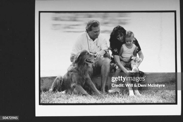 Actor Lee Majors w. His 3rd wife Karen & daughter Nikki relaxing on log w. Their golden retriever dog in front of lake.