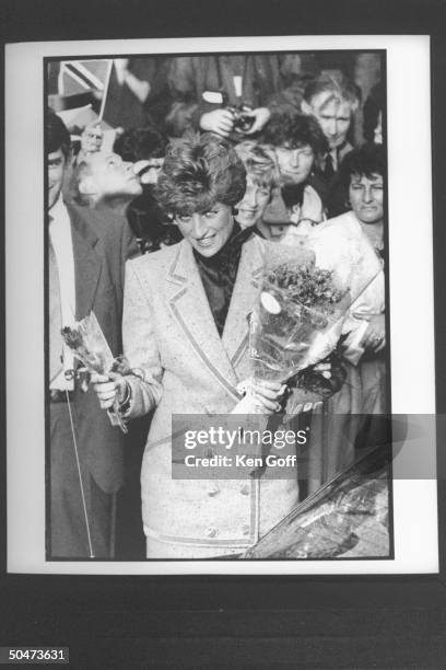 Princess Diana clad in double-breasted wool suit, holding several bouquets of flowers as a group of fans stand behind her during walking tour. North...