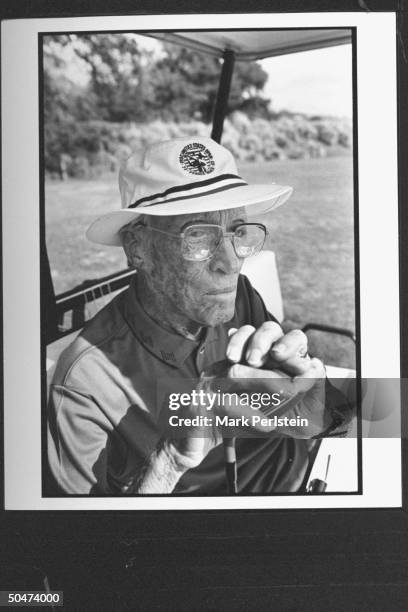 Retired pro golfer Harvey Penick leaning on driver golf club as he sits in golf cart, musing over the success of his book LITTLE RED BOOK, a...