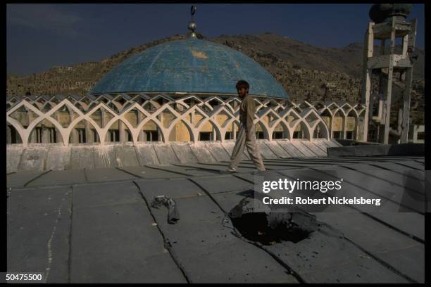 Man on shell holed-marred roof of Shia Hazara mosque under repair for damages sustained in 1993-1994 civil war fighting, in Shia Muslim area of...