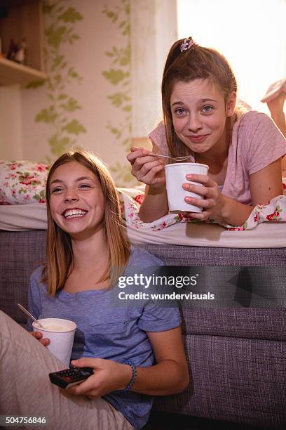 teen girls laughing at tv show while eating ice cream - vertical tv stock pictures, royalty-free photos & images