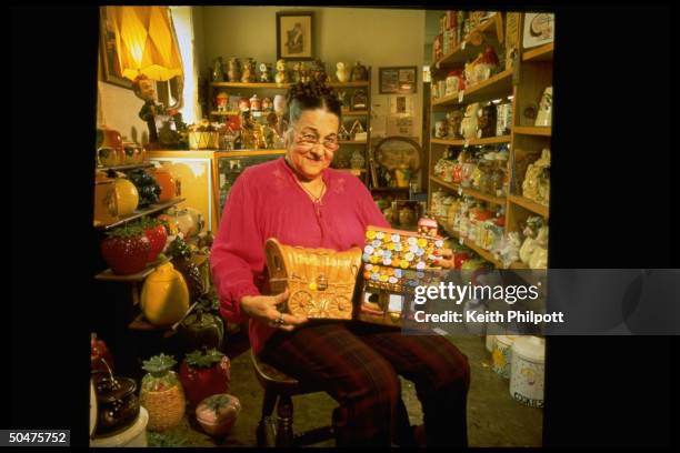 Lucille Bromberek, curator at the Lucille Bromberek's Cookie Jar Museum, w. Two jars in her lap as she sit in chair in the 2,000 piece museum.