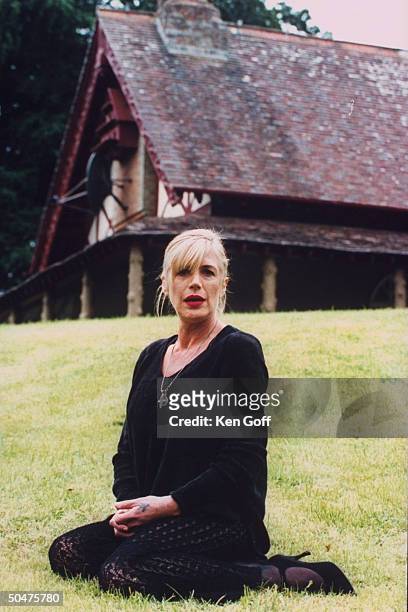 Singer Marianne Faithfull wearing black tunic & lace leggings as she sits on lawn outside her 19th C. Cottage.