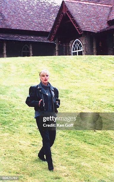Singer Marianne Faithfull wearing black leather jacket as she walks across lawn outside her 19th C. Cottage.