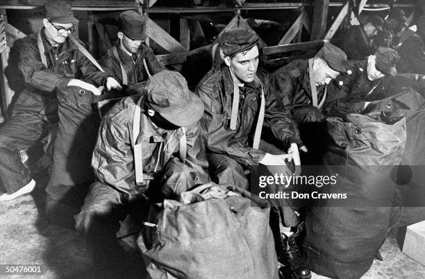 Singer/Army Pvt. Elvis Presley wearing Army fatigues as he tries on shoes while sitting nr. His duffel bag on bench w. Six other new inductees into...