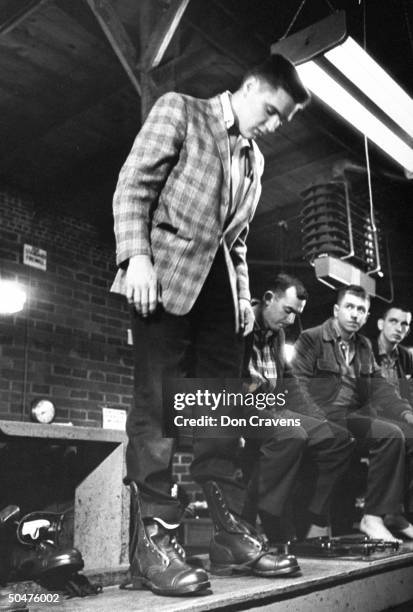 Singer/Army Pvt. Elvis Presley clad in plaid sport coat & slacks as he stands, testing the fit of unlaced Army shoes he has just put on, while being...