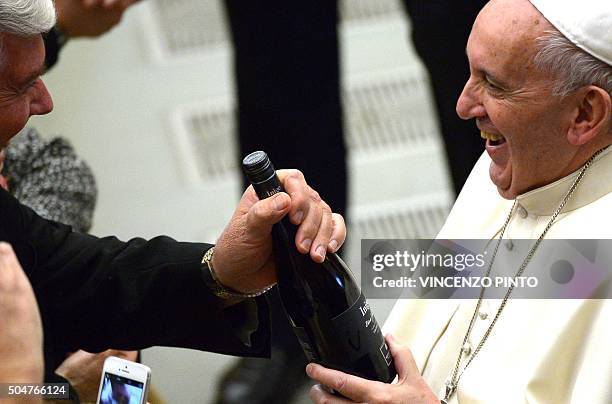 Pope Francis is handed a bottle of wine by a member of the congregation duirng his weekly general audience on January 13, 2016 in the Paul VII hall...