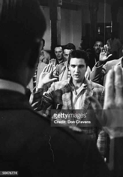 Rock & roll singer Elvis Presley in checkered sport coat, w. R. Hand raised as he is sworn into the Army w. Other inductees by Maj. Elbert Turner at...