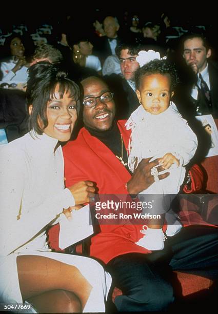 Pop singer Whitney Houston sitting w. Singer husband Bobby Brown, who is holding their infant daughter Bobbi .