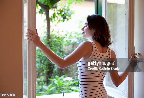 young woman opening window to the garden - fenster offen stock-fotos und bilder