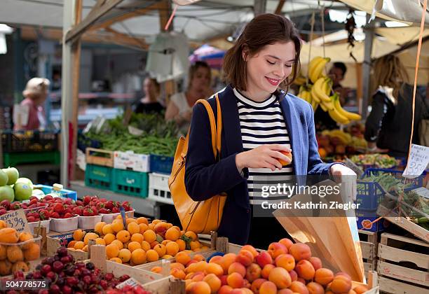 young woman choosing apricots from fruit stand - market stall stock pictures, royalty-free photos & images