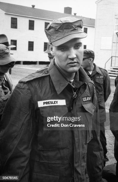 Singer/Army Pvt. Elvis Presley clad in Army fatigues & cap, standing around w. Several inductees outside barracks at Ft. Chaffee reception center.