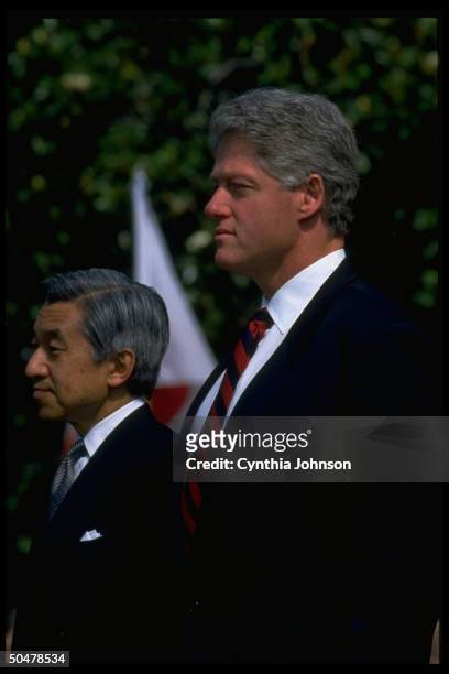 Pres. Bill Clinton & guest Japanese Emperor Akihito striking solemn stance, standing during WH S. Lawn arrival ceremony.