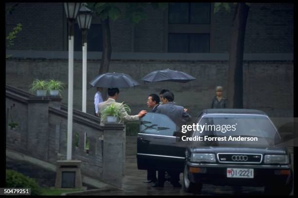 Chinese Premier Li Peng negotiating rain, escorted fr. His limo by umbrella toting aides, arriving for mtg. W. US NSA Tony Lake.