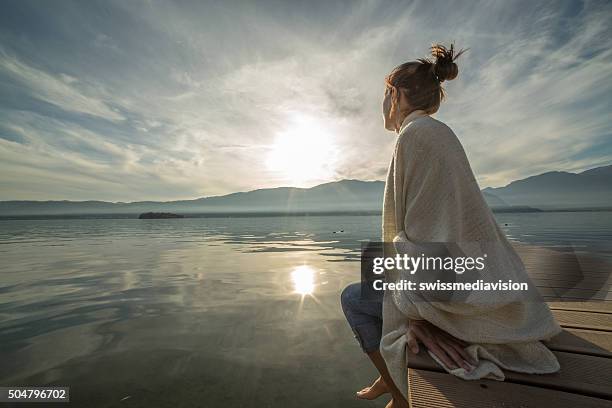 若い女性の桟橋で湖をリラックスさせ、ブランケット、腕時計の夕日 - ポンチョ ストックフォトと画像